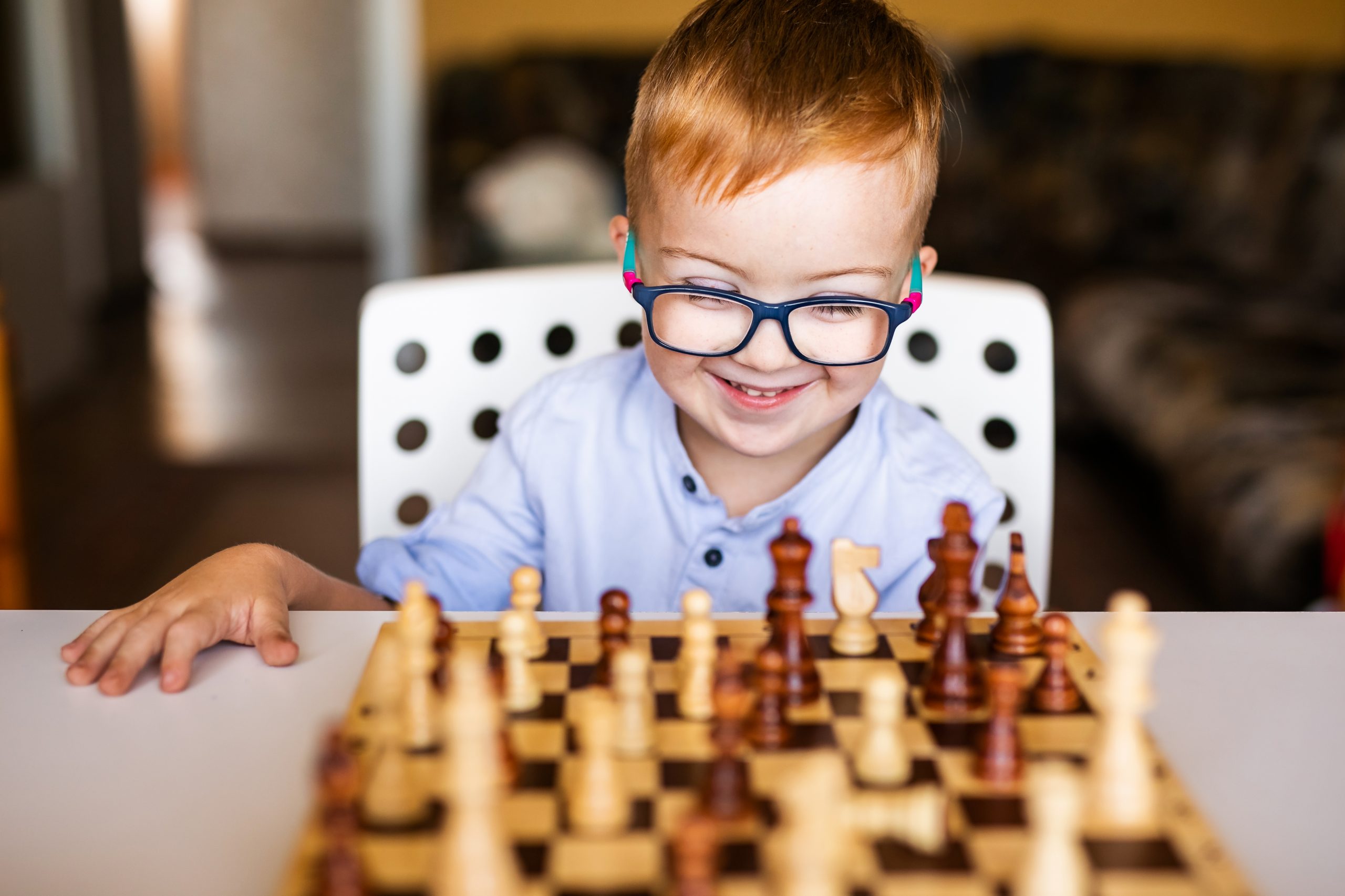 Toddler boy with down syndrome with big blue glasses playing chess in kindergarten